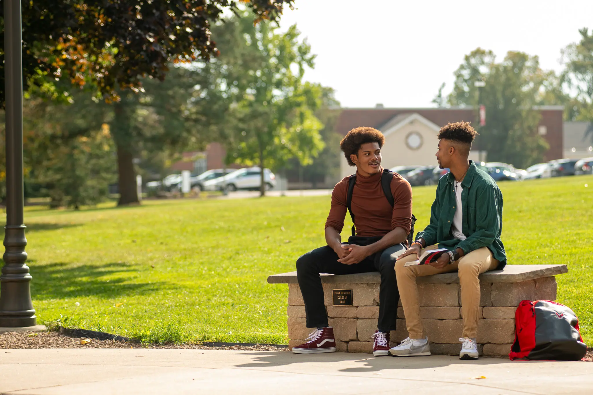 2 young men sit outside on campus and talk