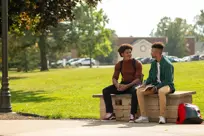 2 young men sit outside on campus and talk
