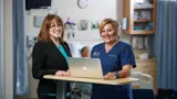 A nurse and nurse leader smile and stand together.